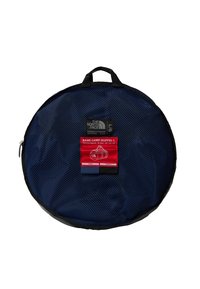 Borsa da viaggio rotonda in rete blu navy con accenti neri, dotata di un'etichetta rossa che dettaglia dimensioni e materiali. Include una maniglia superiore.
