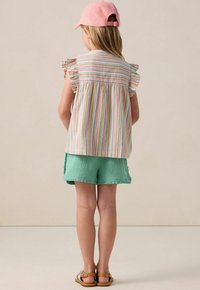 Striped lightweight top with ruffled sleeves, paired with textured mint green shorts. A pink cap complements the outfit. Sandals are worn.