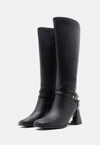 Μαύρες μπότες μέχρι το γόνατο από λείο δέρμα, με χαμηλό τακούνι, κομψό σχέδιο και δύο λουριά με θηλιά για επιπλέον λεπτομέρεια.