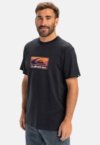 Sort bomulds t-shirt med et farverigt Quiksilver logo grafisk tryk centreret på brystet. Korte ærmer og rund halsudskæring.