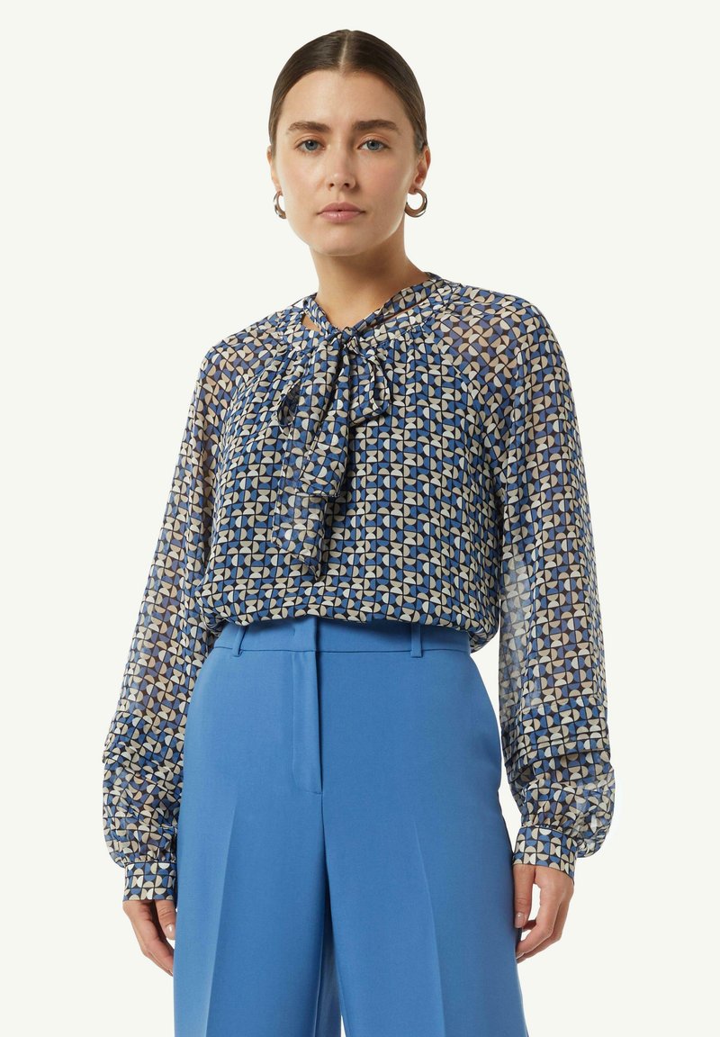 Lichte blauwe blouse met patroon en lange mouwen, strikdetail bij de hals en een semi-doorzichtige textuur, gecombineerd met hooggewaisted blauwe broek.