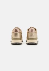 Sneaker beige e marrone chiaro con materiali testurizzati, colletto imbottito, dettaglio del logo e suola in gomma nera a contrasto.