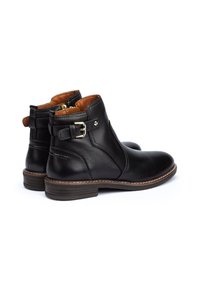 Bottes de cheville en cuir noir avec une fermeture éclair sur le côté, une boucle décorative et une semelle contrastante brune. Intérieur doublé de matériau beige.