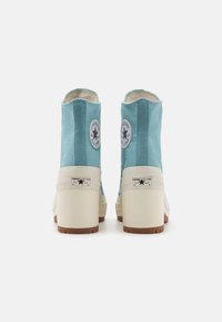 Bottines en toile bleue avec un haut talon blanc, dotées d'un patch logo noir et blanc rond et d'une semelle texturée.