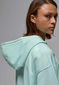 Sudadera verde menta con una capucha grande y suave, mangas raglán y una textura de tela lisa, que muestra un diseño limpio y minimalista.