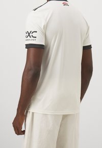 Valkoinen urheilupaita, jossa on lyhyet mustat hihat ja korostukset. Ominaisuuksiin kuuluu pyöreä pääntie ja "EXC Technology" -brändäys vasemmassa hihassa.