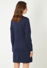 Vestido de manga larga azul marino hecho de una tela suave, con una silueta sencilla, costura trasera y dos bolsillos laterales para un detalle adicional.