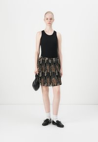 Top sin mangas negro combinado con una falda con pliegues que presenta un patrón de hojas en marrón y negro. Los accesorios incluyen un bolso negro y zapatos negros con calcetines blancos.