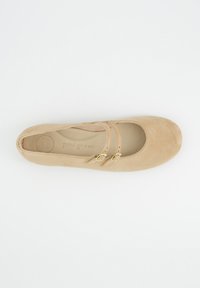 Ballerine en daim beige avec un bout arrondi. Dotée de deux brides décoratives et d'accents en métal doré. Doublure intérieure lisse pour plus de confort.