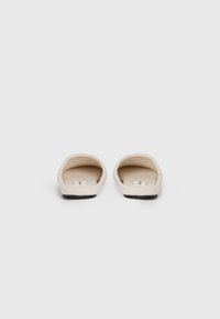 Lichtbeige instappantoffels met een gladde, zachte stof bovenkant en een zwarte rubberen zool. Minimalistisch design zonder extra patronen of versieringen.
