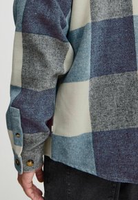 Blau- und graues Karohemd mit geknöpftem Ärmel. Hergestellt aus strukturierter Stoff mit einer Mischung aus großen Karomustern und kontrastierenden Farben.