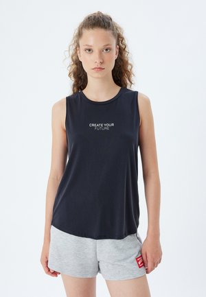 Donker marineblauw mouwloos topje met de tekst "CREATE YOUR FUTURE", gemaakt van gladde stof. Gecombineerd met grijze shorts met een klein rood etiket.