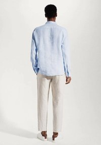 Camisa de lino de manga larga de color azul claro con un dobladillo curvado. Combinada con pantalones de lino color crema y zapatillas blancas con acentos marrones.