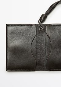 Černá kožená peněženka s texturovaným povrchem, obsahující dvě přihrádky a kovový kroužek na straně. Hladké okraje s minimálním zdobením.