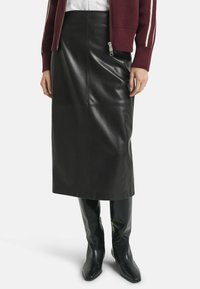 Zwarte leren midi-rok met een strakke afwerking en paneelontwerp, gecombineerd met knielange zwarte leren laarzen voor een gepolijste uitstraling.