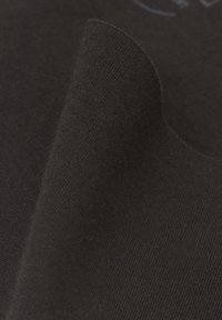 Gros plan d'un tissu doux et sombre avec une texture tricotée visible et des plis doux créant une surface lisse et courbée.