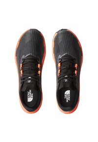 Baskets de sport noires avec une tige en maille texturée, accents orange sur la semelle et les lacets, et une marque bien visible sur la languette et la semelle intérieure.