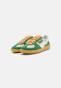 Sneaker in suede verde e beige chiaro con lacci arancioni, punta arrotondata, dettaglio del logo bianco e suola in gomma. Design testurizzato su tutta la superficie.
