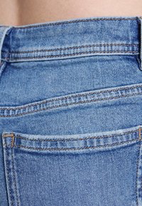 Jeans de ganga azuis com uma textura suave, apresentando uma cintura alta, dois bolsos traseiros e detalhes de costura contrastantes.