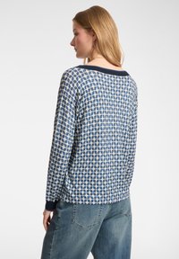 Maglia leggera a maniche lunghe in blu e crema con un motivo geometrico, dotata di colletto e polsini blu navy. Tessuto morbido e strutturato.