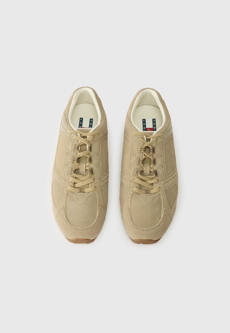 Beige athletic shoes with a textured suede upper, round toe, and lace-up closure. Features contrasting stitching and rubber outsole.