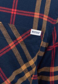 Flanellen overhemd in marineblauw met een rood en beige geblokt patroon. Voorzien van een klein wit etiket met het "MUSTANG" logo. Zachte, gestructureerde stof.