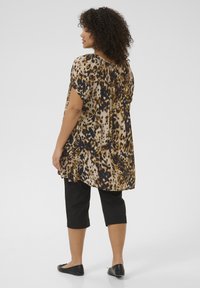 Tunique imprimée avec un motif léopard dans des tons beige, marron et noir ; manches courtes ; coupe ample ; associée à un pantalon capri noir et des chaussures plates.