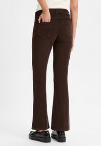 Bruine flared corduroy broeken met een gestructureerde afwerking, voorzien van achterzakken en een middelhoog tailleband. Gekocht met zwarte platform schoenen.