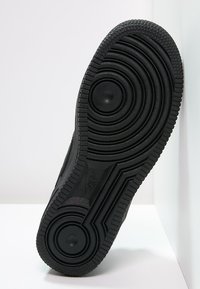 Černá podrážka tenisky s texturovaným vzorkem a kruhovými akcenty. Vyrobena z gumy, s hladkými a drsnými sekcemi.