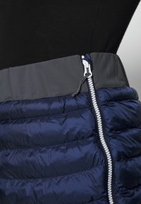 Marinblå pufferkjol med horisontella quiltade sektioner, grå midjeband och vit dragkedjedetalj. Slät textur och lätt material.