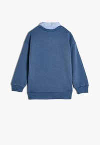 Sweatshirt blu con scollatura rotonda e maniche lunghe. Presenta uno strato sottostante di colore blu più chiaro, con colletto. Realizzato in tessuto morbido con una finitura testurizzata.