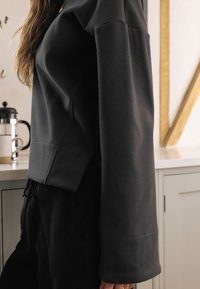 Dunkelgraues Sweatshirt mit lockerer Passform, rundem Ausschnitt, langen Ärmeln und weicher Textur. Kombiniert mit schwarzen Cordhosen.