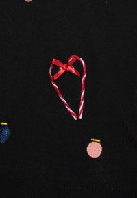 Mustapaita, jossa on brodeeratut kuvastot, mukaan lukien punavalkoinen raidallinen sydän ja kaksi pyöreää koristetta sinisessä ja vaaleanpunaisessa.