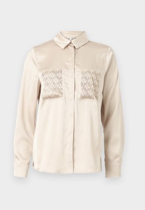Cămașă cu nasturi din satin bej, cu mâneci lungi, având două buzunare decorative cu modele geometrice decupate pe piept.
