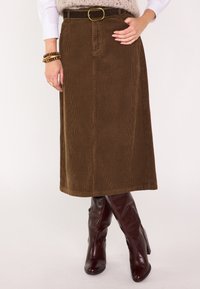 Gonna midi in velluto a coste marrone con cintura con fibbia circolare, abbinata a stivali bordeaux lucidi al ginocchio. Texture a coste verticali visibile.