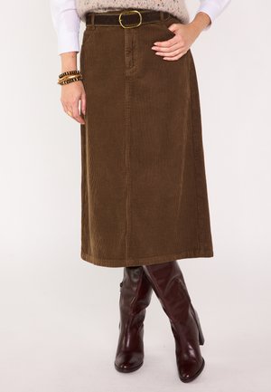 Brauner Cord-Midirock mit einem Gürtel, der eine runde Schnalle aufweist, kombiniert mit glänzenden burgunderroten kniehohen Stiefeln. Vertikale gerippte Textur sichtbar.