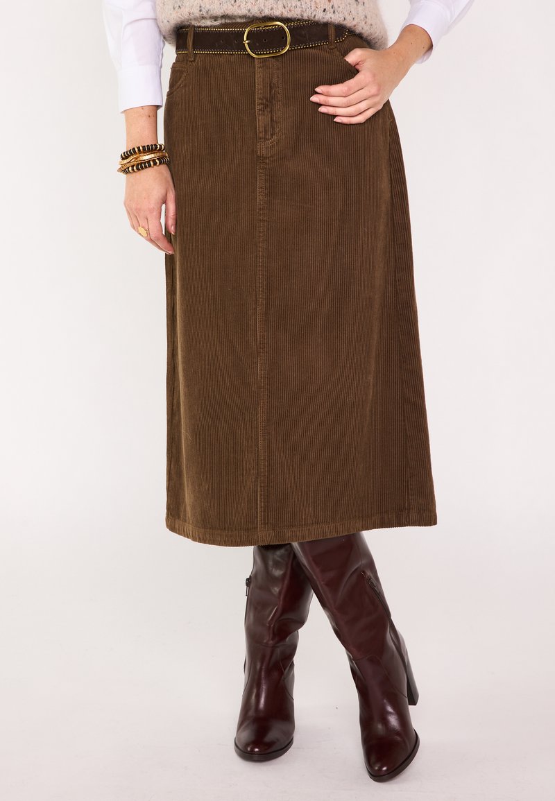 Gonna midi in velluto a coste marrone con cintura con fibbia circolare, abbinata a stivali bordeaux lucidi al ginocchio. Texture a coste verticali visibile.