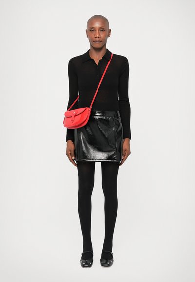 Black long-sleeve top, shiny black mini skirt, black tights, and black shoes with decorative accents; red crossbody bag.