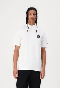 Tricou alb din bumbac cu o croială obișnuită, m�âneci scurte și un logo rotund negru pe piept. Are decolteu rotund și branding adidas.