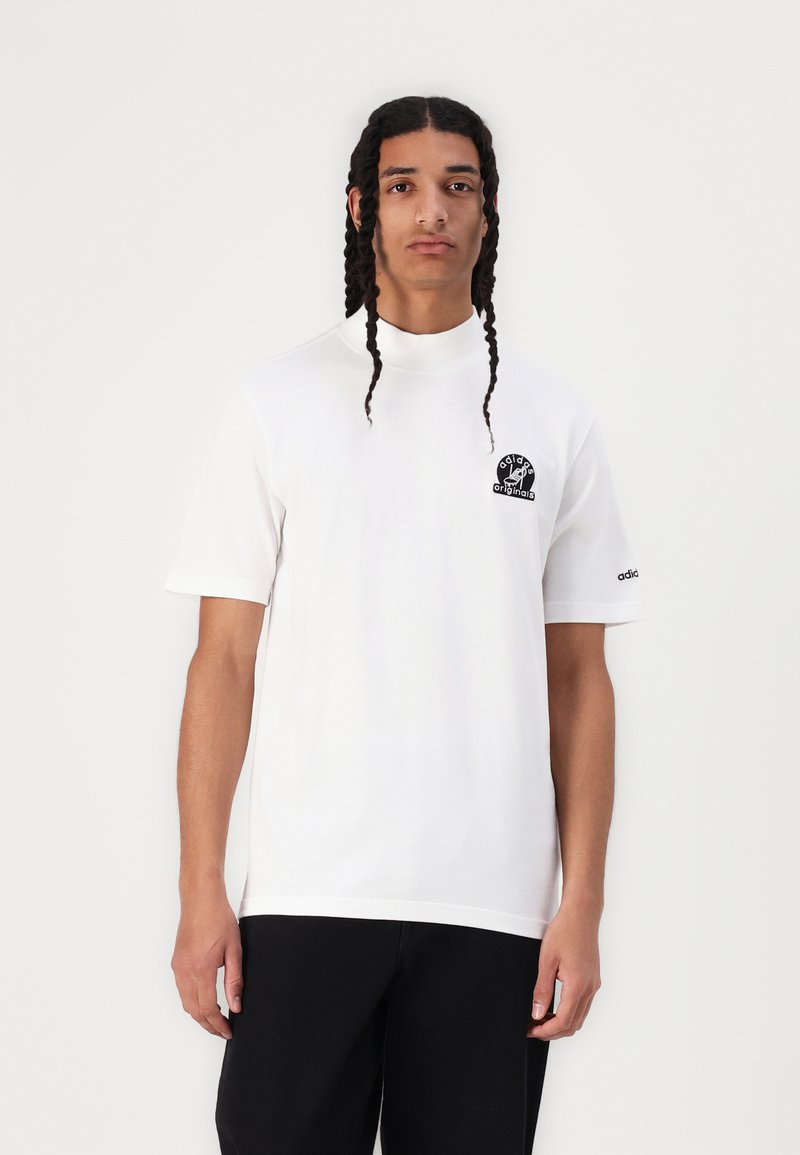 Fehér pamut póló, normál fazonú, rövid ujjú, fekete kerek logóval a mellkason. Kerek nyakkivágása és adidas márkajelzése van.