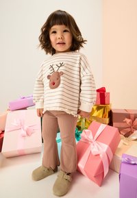 Striped cream sweatshirt with reindeer appliqué, paired with light pink ribbed pants and gray suede clogs. Surrounded by colorful gift boxes.