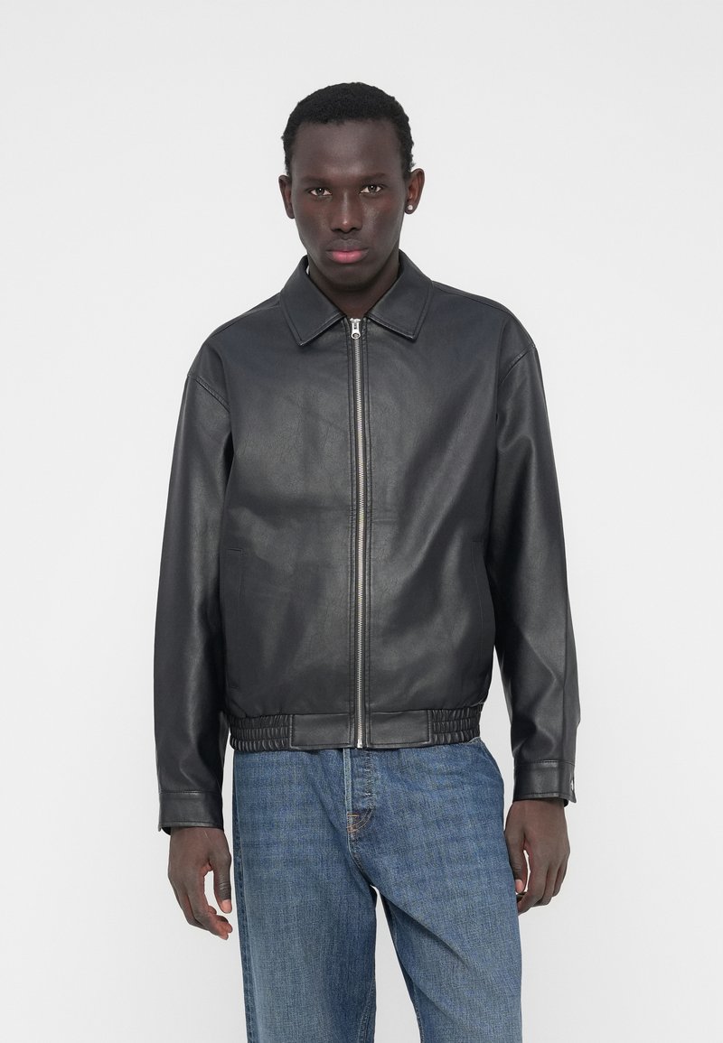 Veste en cuir noir avec un col et une fermeture éclair à l'avant. Dotée d'une taille et de poignets élastiqués, d'une texture lisse et d'une coupe ajustée.