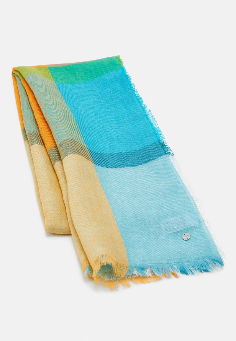 Écharpe colorée pliée avec de grands blocs turquoise, jaune, vert et orange, présentant des bords légèrement effilochés et une petite étiquette métallique ronde.