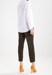 Vit långärmad skjorta, svarta mönstrade byxor med guldackenter, och orangea mockahögklackade skor, sedd från baksidan.