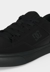 Baskets noires DC avec lacets, semelle texturée et logo sur le côté, vues en gros plan sous un angle.