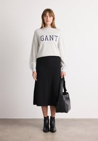 Grijze sweatshirt met "GANT" logo, zwarte midi rok, zwarte enkellaarsjes en een zwarte handtas. Soepele texturen en modern casual ontwerp.