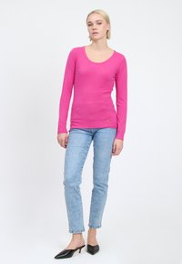 Top rosa a maniche lunghe aderente con scollatura a barco; indossato con jeans in denim azzurro chiaro e mule nere a punta.