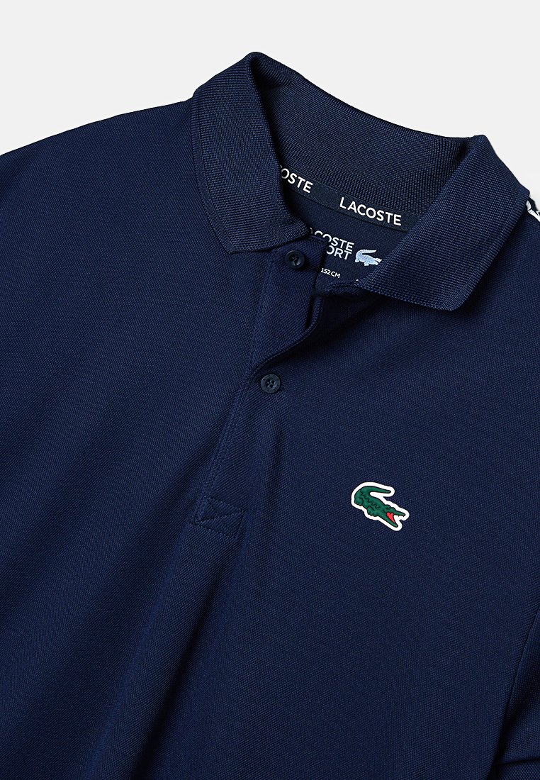 Dunkelblaues Polohemd aus strukturiertem Stoff, mit flachem Kragen, Drei-Knopf-Leiste und kleinem grünen Lacoste-Krokodil-Logo auf der Brust.