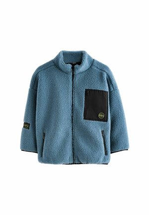 Blå fleecejakke med høj krave, sort lynlåslomme på brystet, to lynlåslommer i siderne og mærke på venstre ærme.