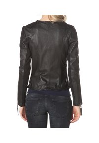 Femme portant une veste en cuir noire ajustée et un jean bleu foncé, vue de dos sur fond blanc.